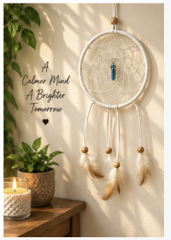 A white dreamcatcher wall hanging with a blue feather accent and hanging beads, displayed on a beige wall in a styled room scene with a candle, potted plants, and the text 'A Calmer Mind A Brighter Tomorrow'.