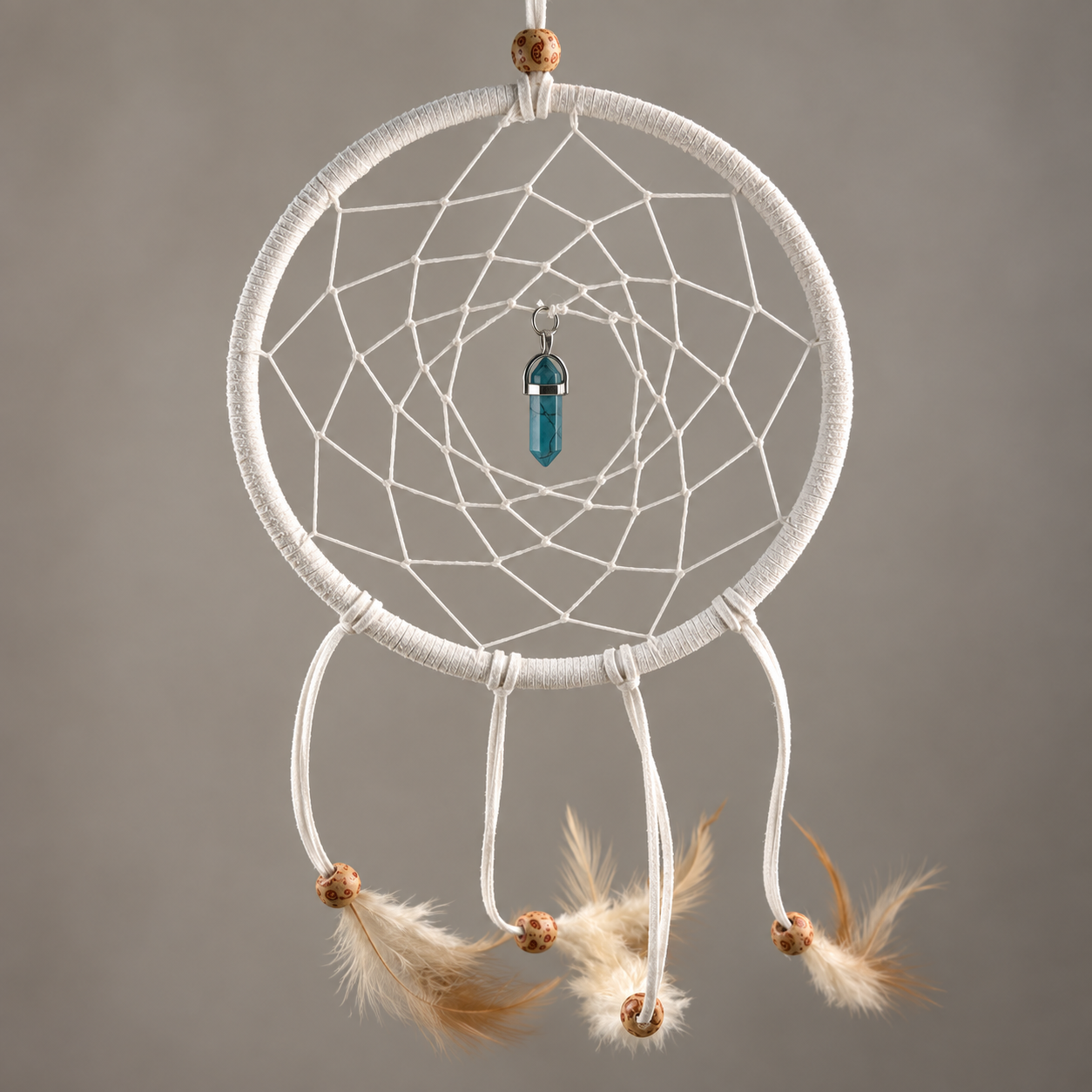 A white dreamcatcher with a wrapped circular hoop, intricate webbing, a small blue glass bead in the center, and three dangling cords ending in tan feathers and wooden beads, shown against a plain gray background.