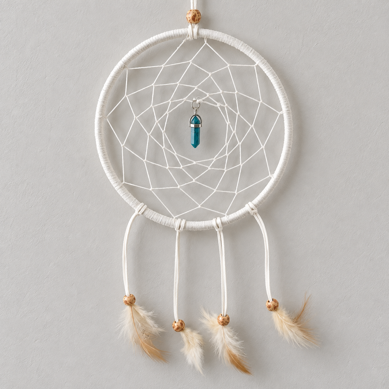 A white dreamcatcher with intricate webbing, three hanging white cords with tan and white feathers, and a small blue bead charm in the center, hanging against a light gray wall.