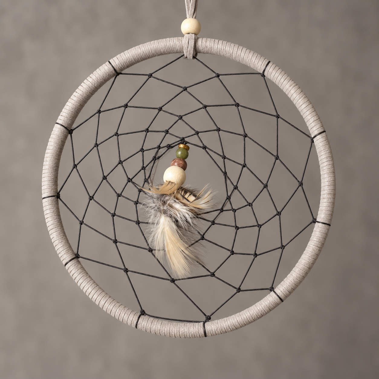 A bohemian-style dreamcatcher with a light beige wrapped hoop, black webbing, and a central feather ornament