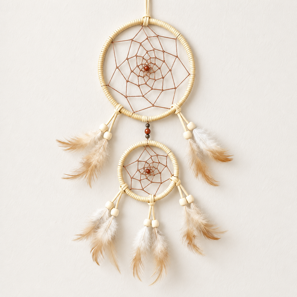 A double-ring dreamcatcher wall hanging with natural beige wrapped hoops, brown thread webs, cream beads, and tan and white feathers, shown against a plain off-white background.
