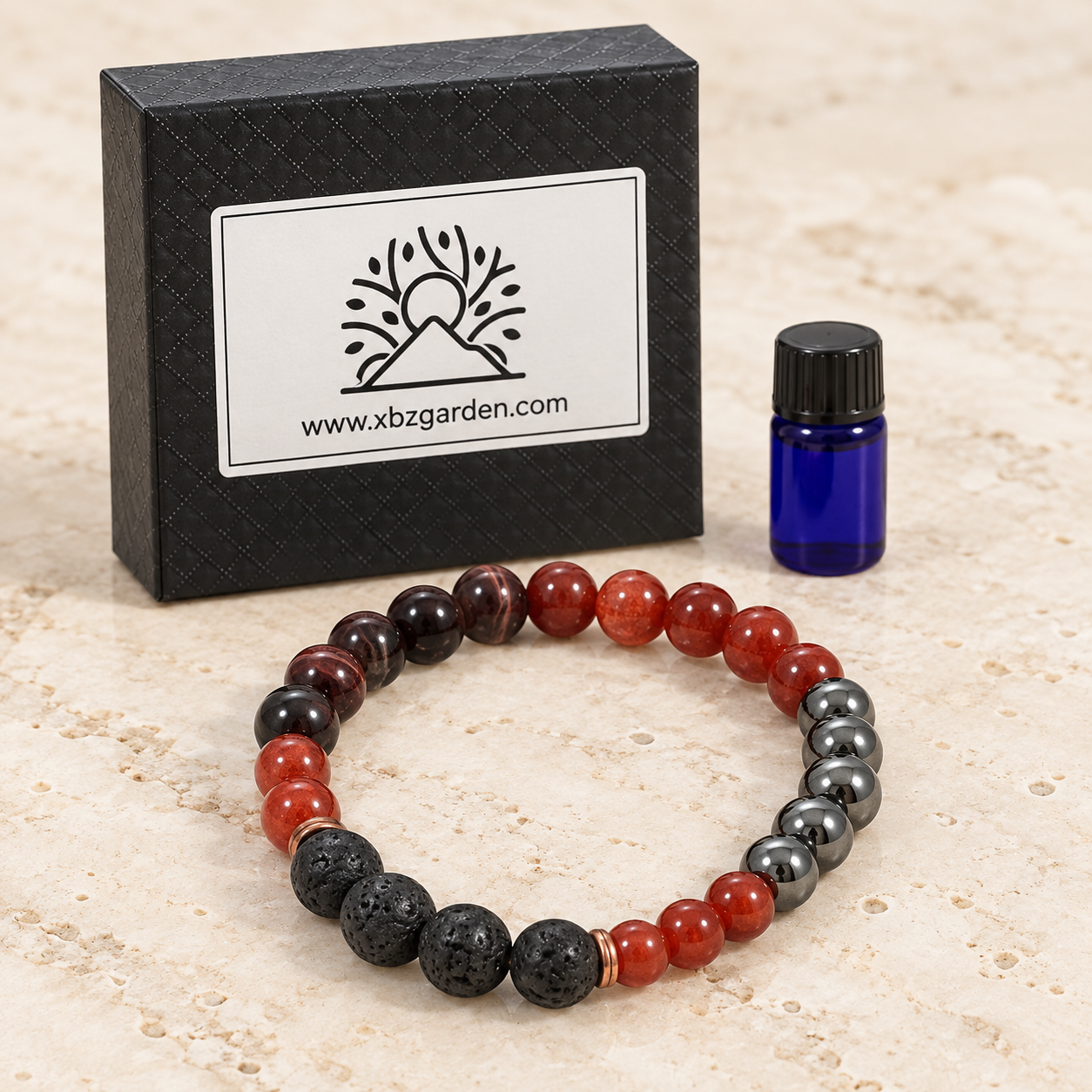 A beaded stretch bracelet with red carnelian, dark gray lava stone, and black wood beads, displayed with its black branded gift box and a small blue essential oil bottle on a light stone surface.