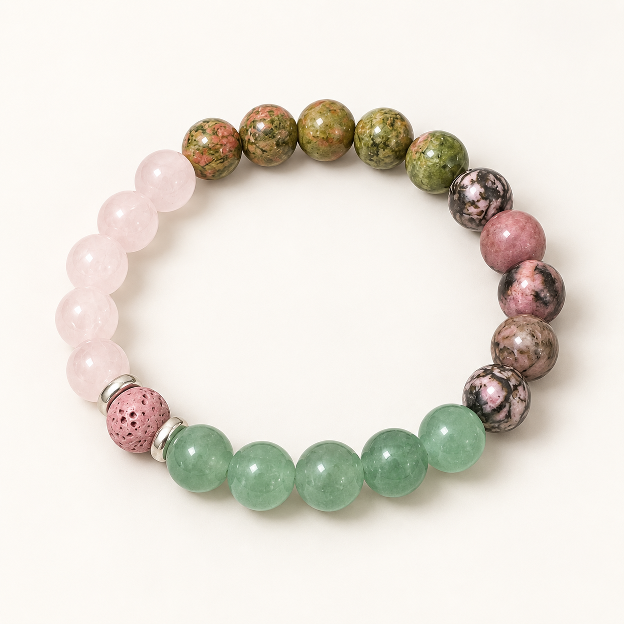 A beaded stretch bracelet featuring light pink rose quartz beads, green jade-like round beads, mottled green and pink jasper beads, and dark marbled beads, with a pink porous accent bead and silver spacer rings, shown on a light cream background.