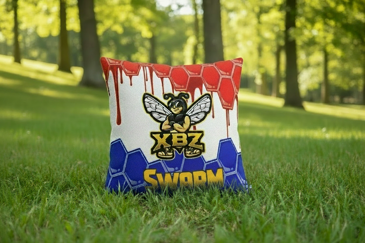 XBZ Swarm cornhole bags in red, white and blue with bee logo on grass